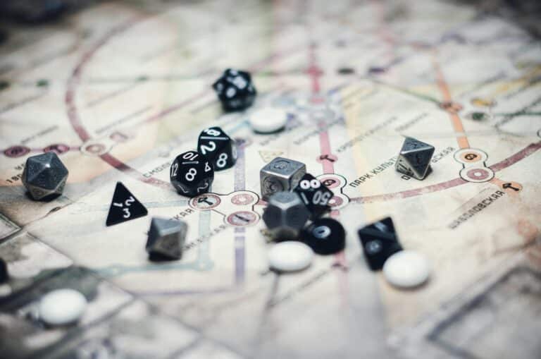 Assorted dice of various shapes and colors, including black and gray, are scattered over a map indicative of a tabletop RPG setting, with lines and circles hinting at a Pathfinder RPG game. White tokens are interspersed among the dice, ready for adventure.